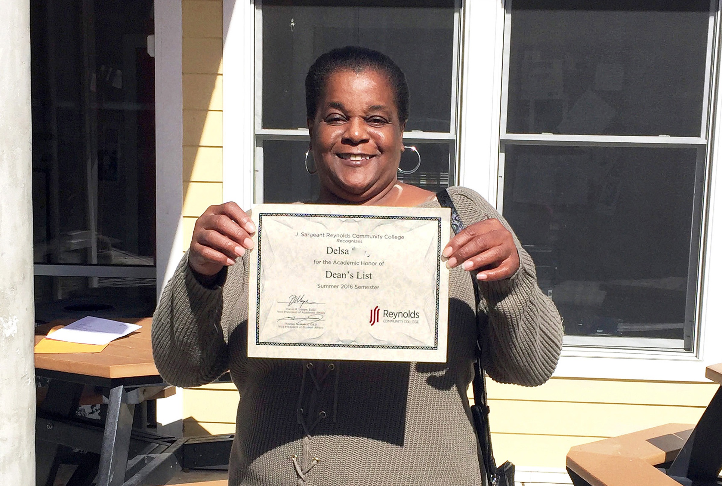 Image of Delsa, an African-American woman, smiling and holding up her Dean's List certificate from Reynolds Community College