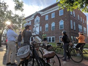 People standing beside bikes looking at a three-story brick building in Church Hill neighborhood